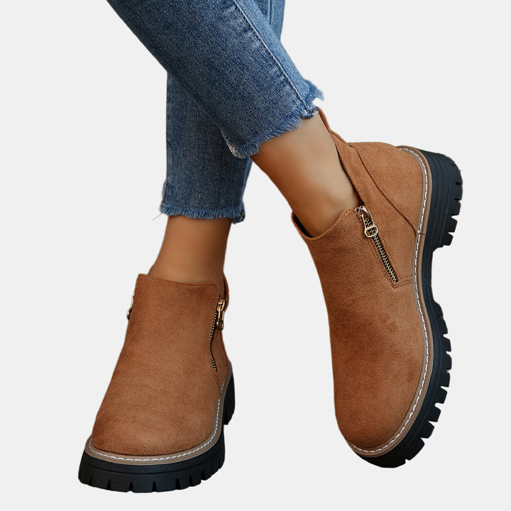 Brown suede ankle boots with side zipper and tan stitched trim, chunky lug sole.