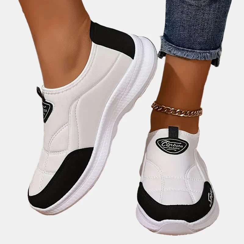 White slip-on sneakers with black trim, white sole, and logo heel patch