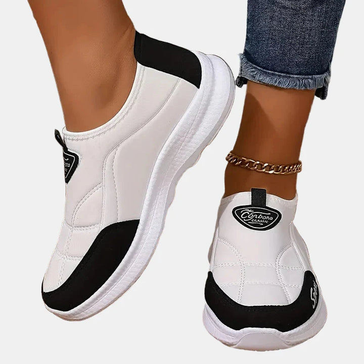White slip-on sneakers with black trim, white sole, and logo heel patch