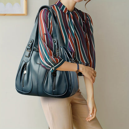 Women’s casual shoulder bag in blue worn on shoulder with top handles and strap.