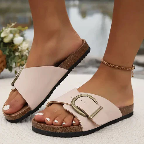 Orthopedic sandals in cream with adjustable strap and round buckle over a dark sole.