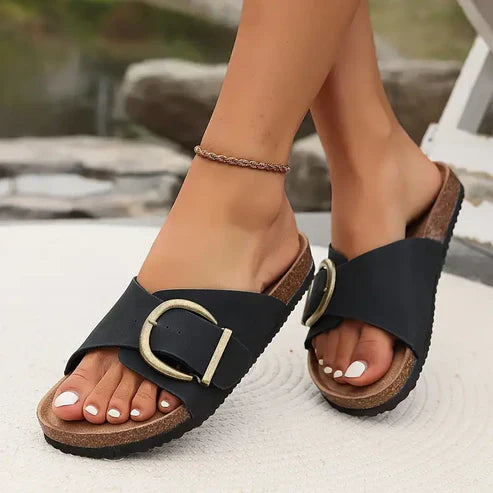 Orthopedic sandals in black with adjustable strap and round buckle over a dark sole.