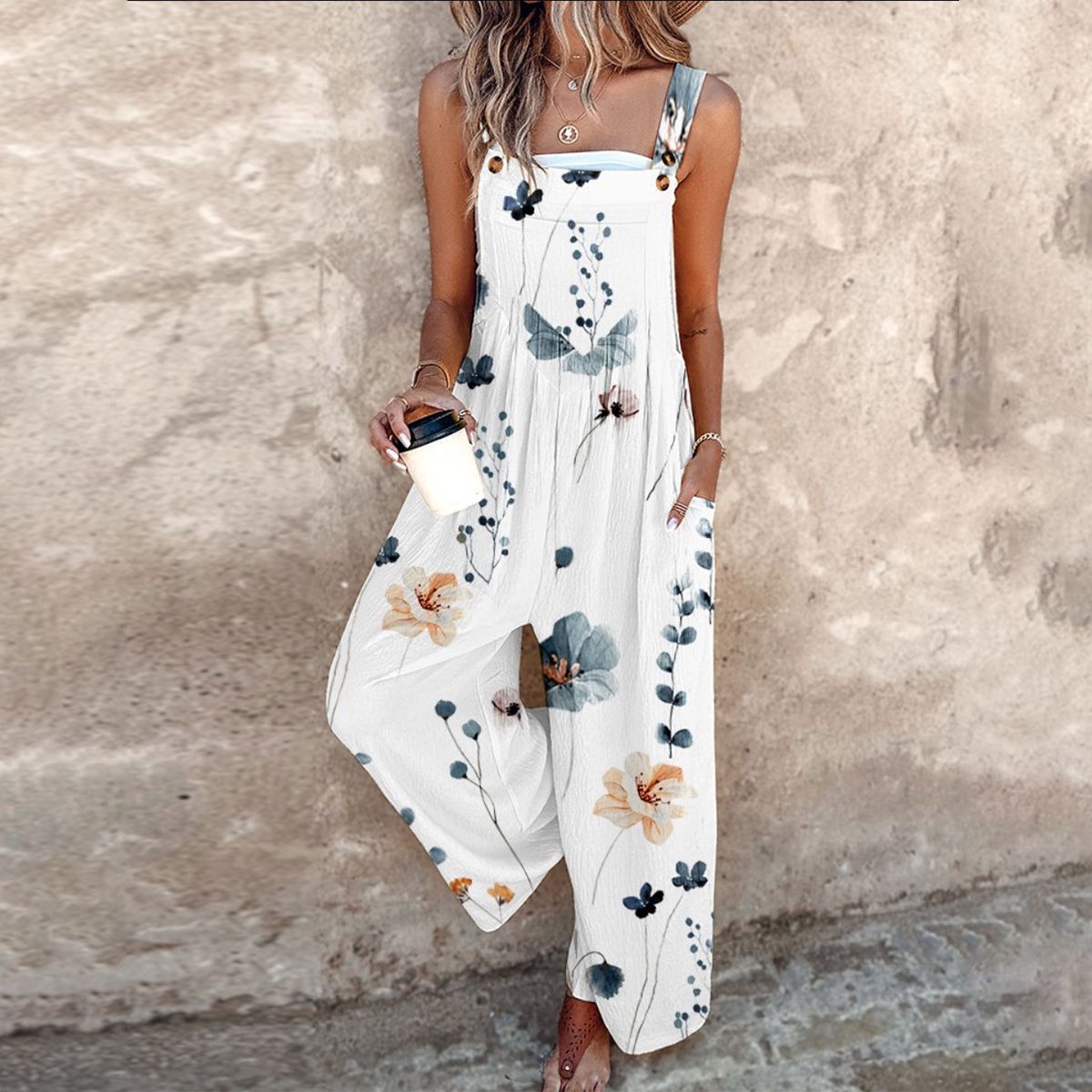 White sleeveless floral overalls with blue leaves and orange flowers, wide legs.
