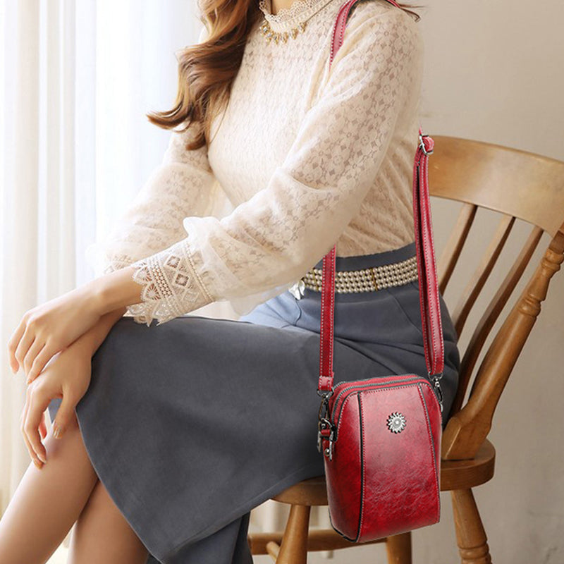Red mini crossbody handbag with zipper closure and sunburst emblem on model.