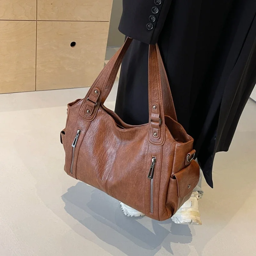 Brown large shoulder bag carried with crossbody strap and dual front zippers