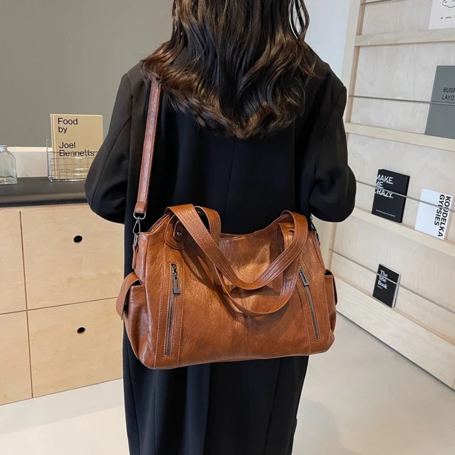 Brown large shoulder bag held crossbody, featuring dual front zip pockets