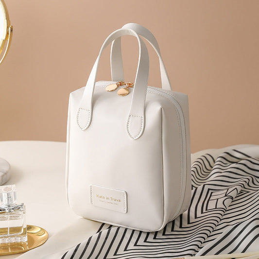White travel bag tote with top handles, gold charm, and front label pocket