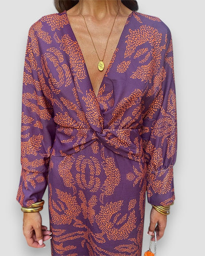 Purple V-neck wrap dress with long sleeves, coral button-tie waist, and ornate print.
