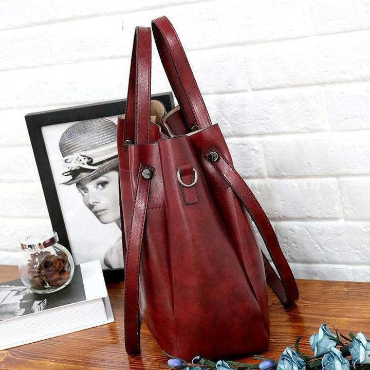 Burgundy tote bag with shoulder straps, front tab details, and side pockets