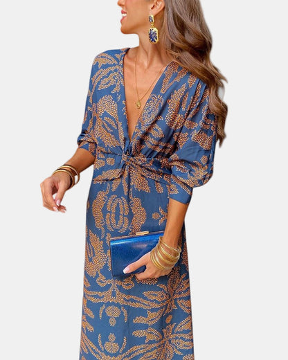 Blue V-neck wrap dress with long sleeves, gold button-tie waist, and ornate print.