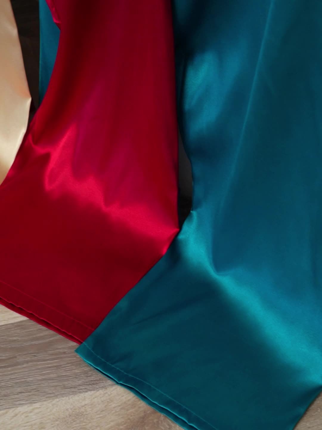 Satin fabric close-up showing red and peacock blue panels with smooth sheen