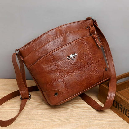 Brown leather crossbody bag with zip closure, front logo, and adjustable shoulder strap.
