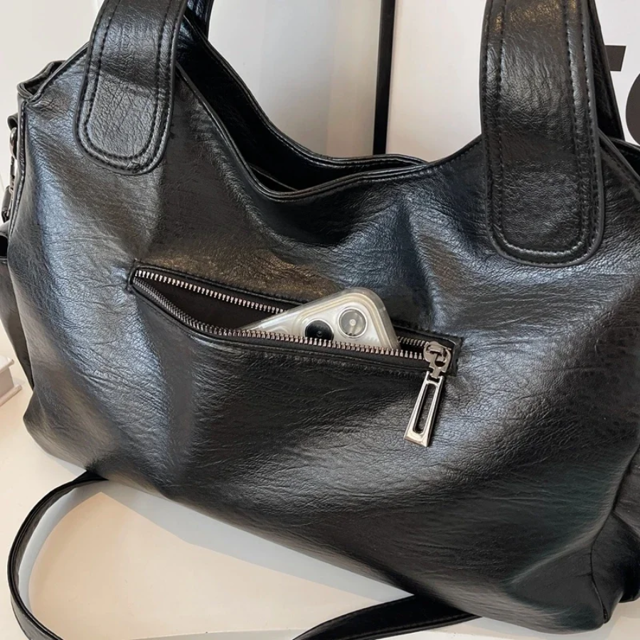 Black leather shoulder bag close-up with front zip pocket and top handle stitching