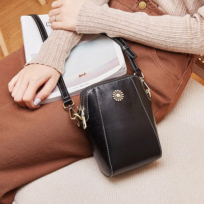 Black compact mini handbag with crossbody strap, zipper closure, and sunburst front emblem.