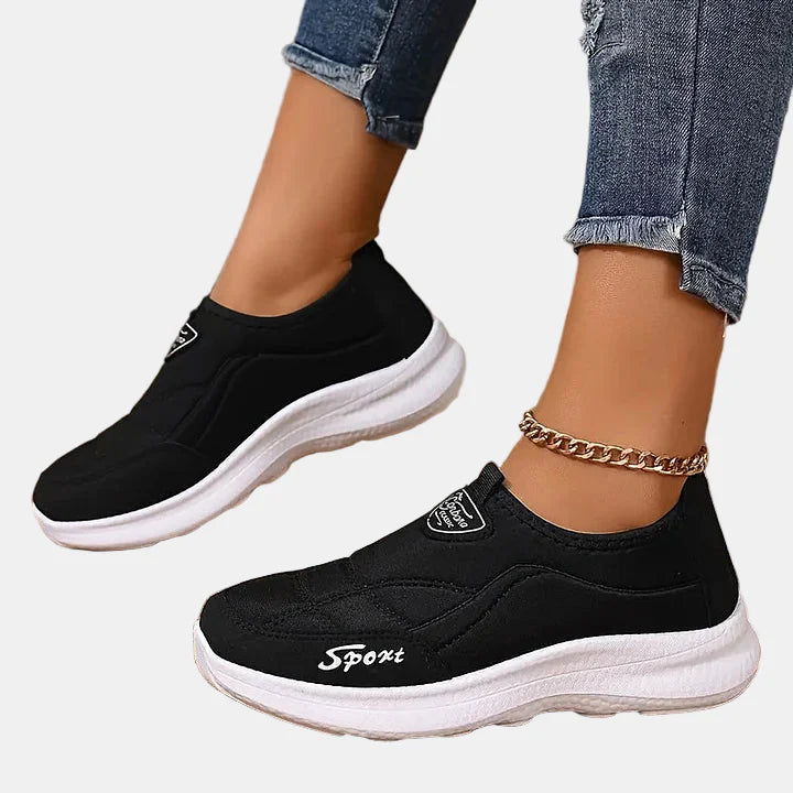 Black slip-on sneakers with white sole, textured panels, and logo patch