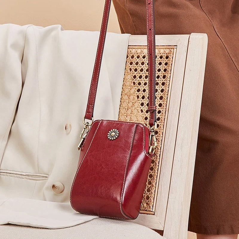 Red compact mini handbag with crossbody strap, zipper closure, and sunburst front emblem.
