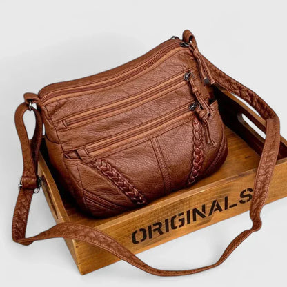 Women’s brown leather shoulder bag with braided front detail and multiple zip pockets.