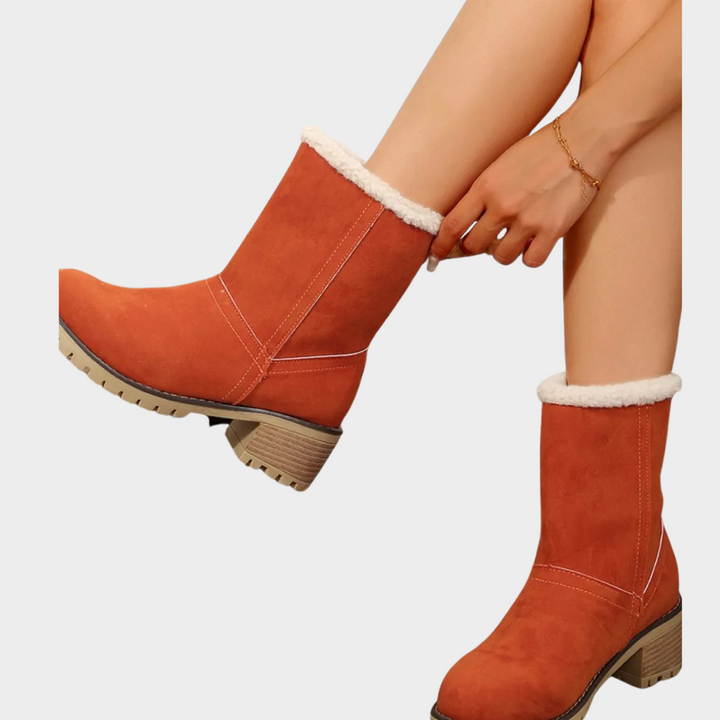 Orange mid-heel winter boots with sherpa trim, diagonal seam detail, and lug outsole