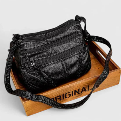 Women’s black leather shoulder bag with braided front detail and multiple zip pockets.