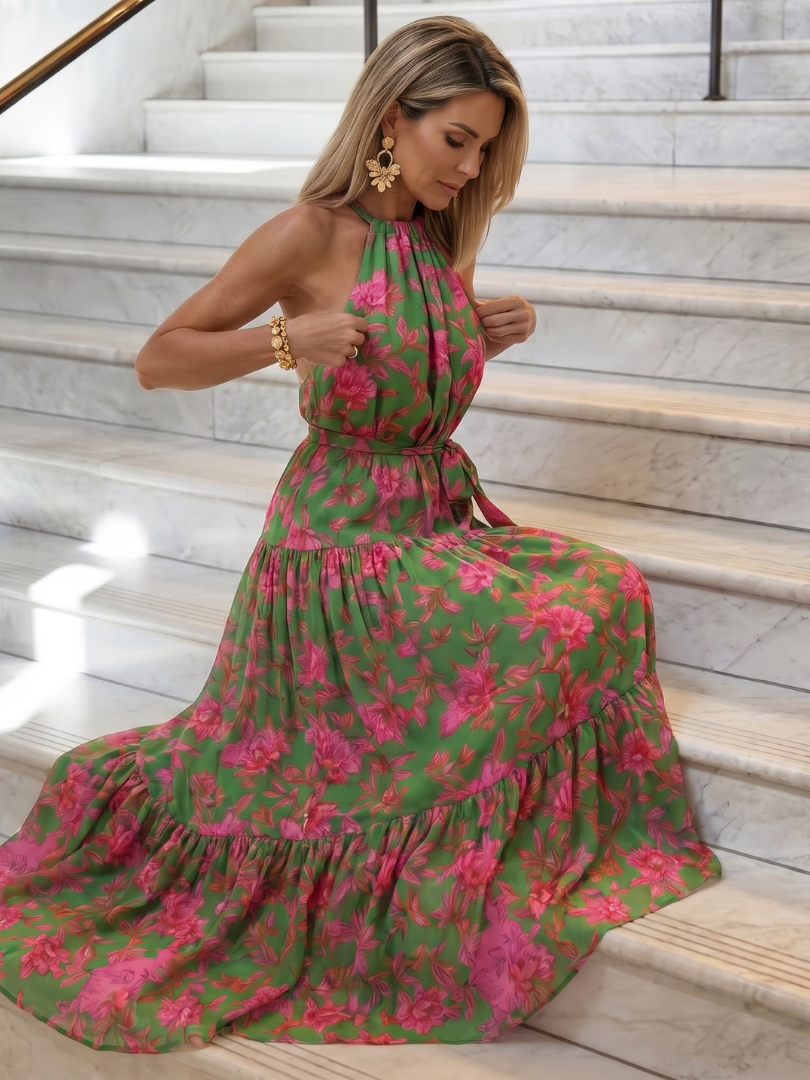Floral halter midi dress with flowing tiered skirt, ruched waist, and pink blooms on green.