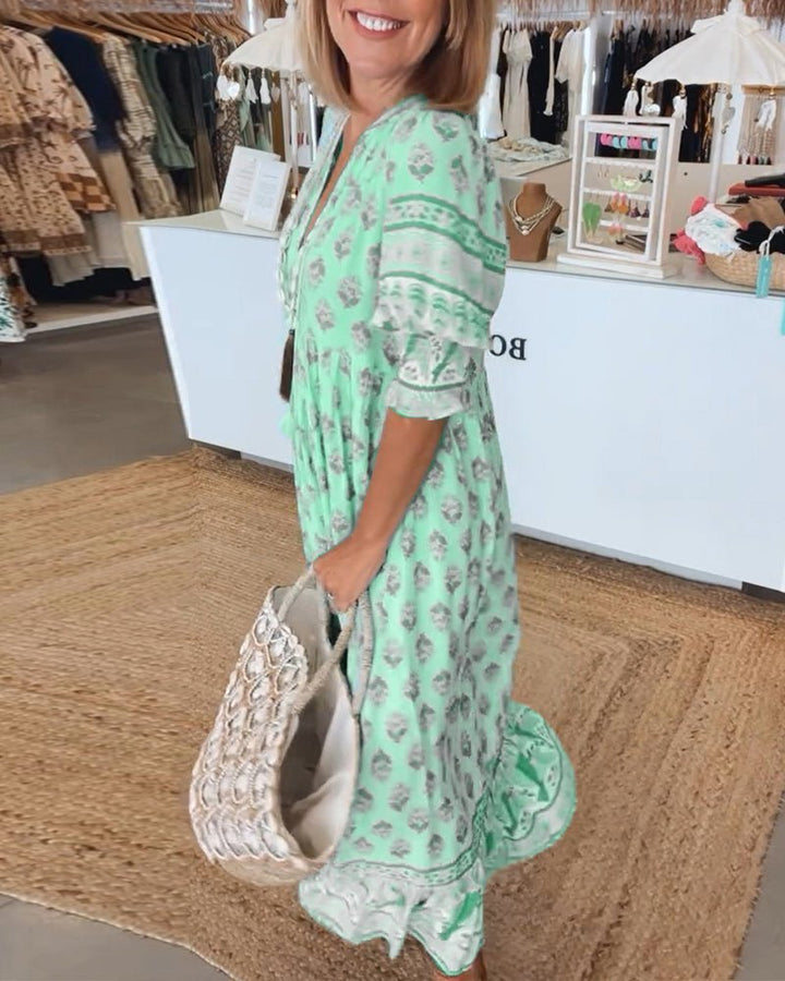 Green floral V-neck tiered dress with ruffle sleeves, side view holding a woven bag