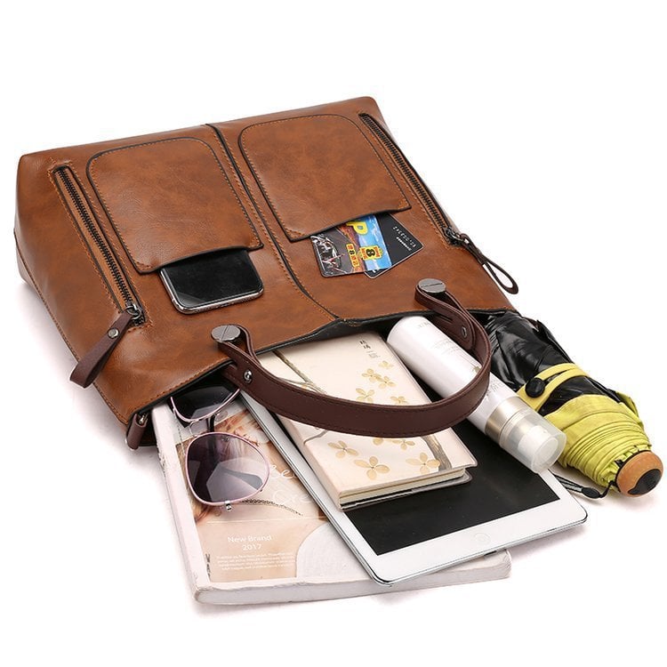 Brown PU leather crossbody tote with front zip pockets and top handle, shown with contents.