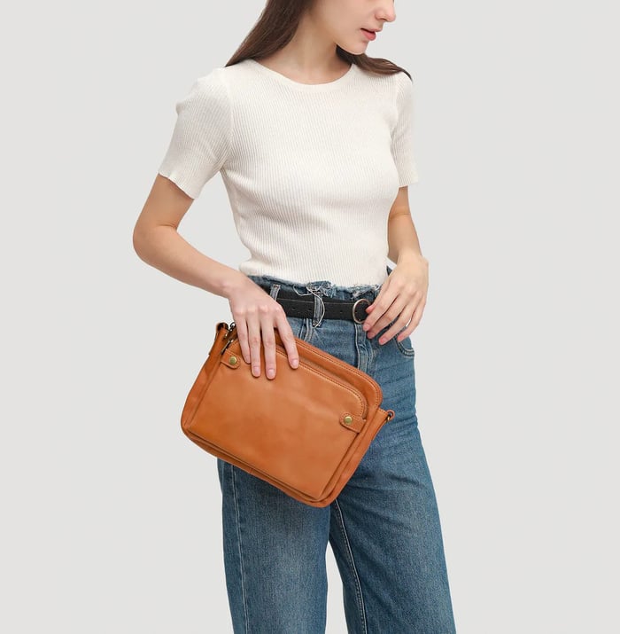 Orange crossbody bag held by model with zip front pockets and adjustable shoulder strap