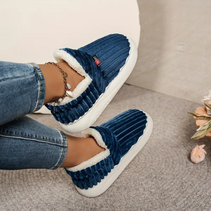 Blue comfort slippers with white shearling trim, ribbed upper, and chain bracelet