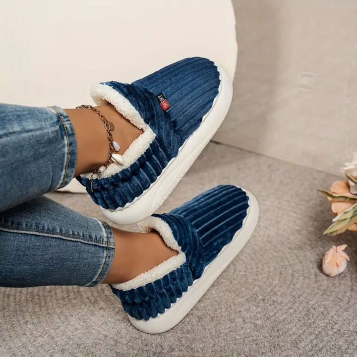 Blue comfort slippers with white shearling trim, ribbed upper, and chain bracelet