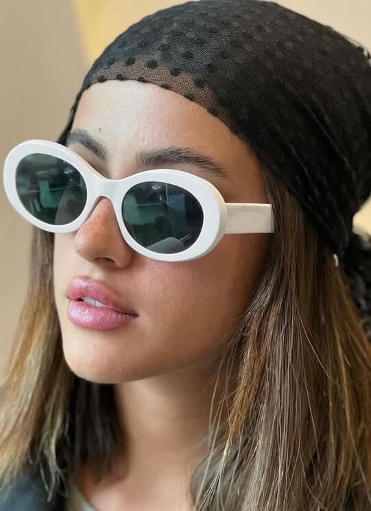 White oval sunglasses with tinted lenses and curved frame, close-up on model