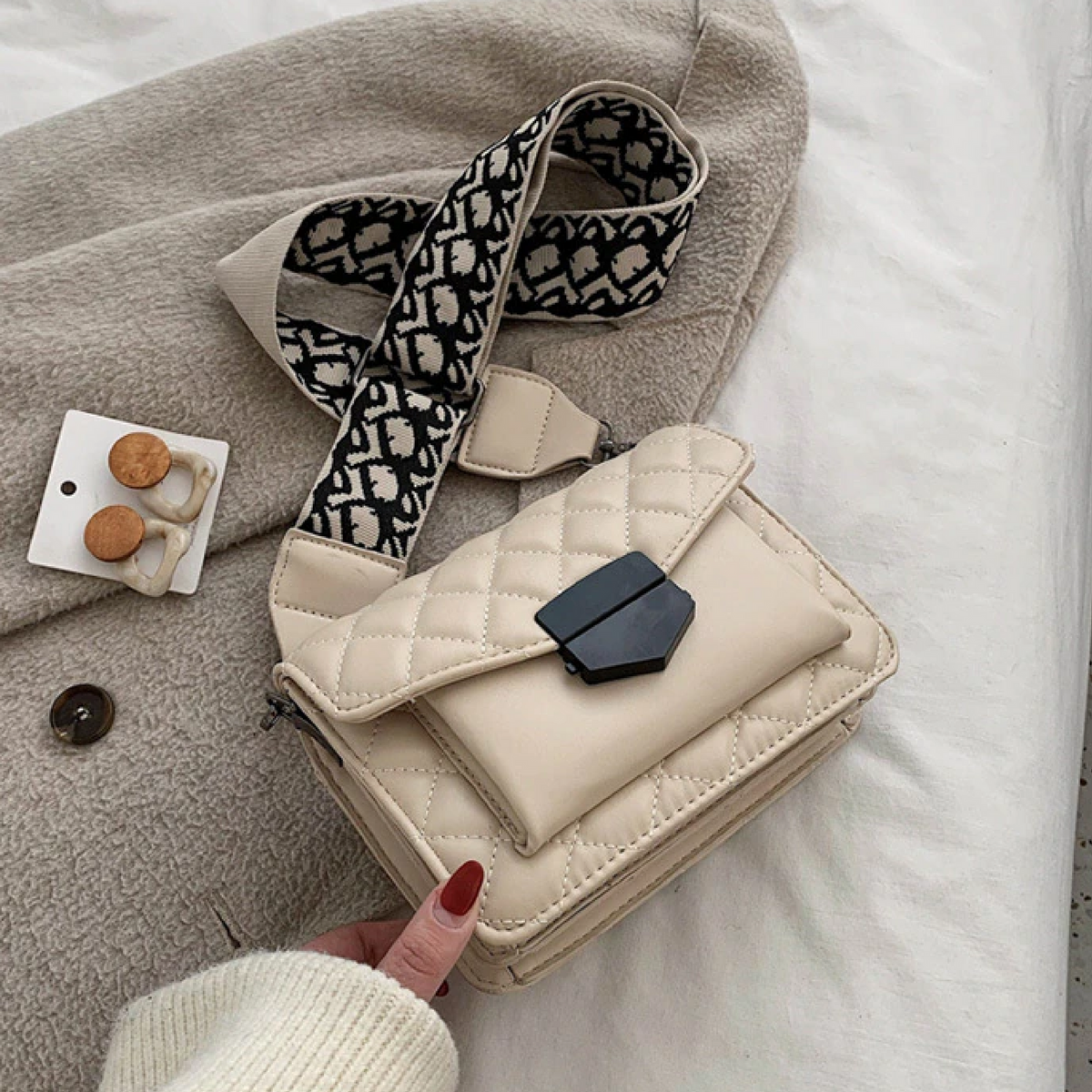 Beige quilted luxury shoulder handbag with black logo-pattern strap and flap closure.