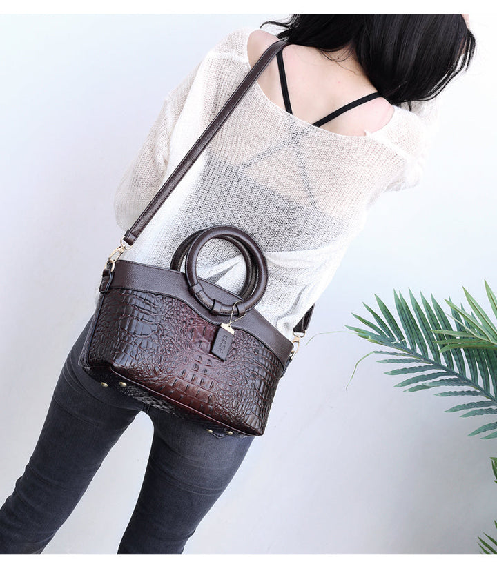 Medium brown croc-embossed handbag worn crossbody with wide strap and gold details.