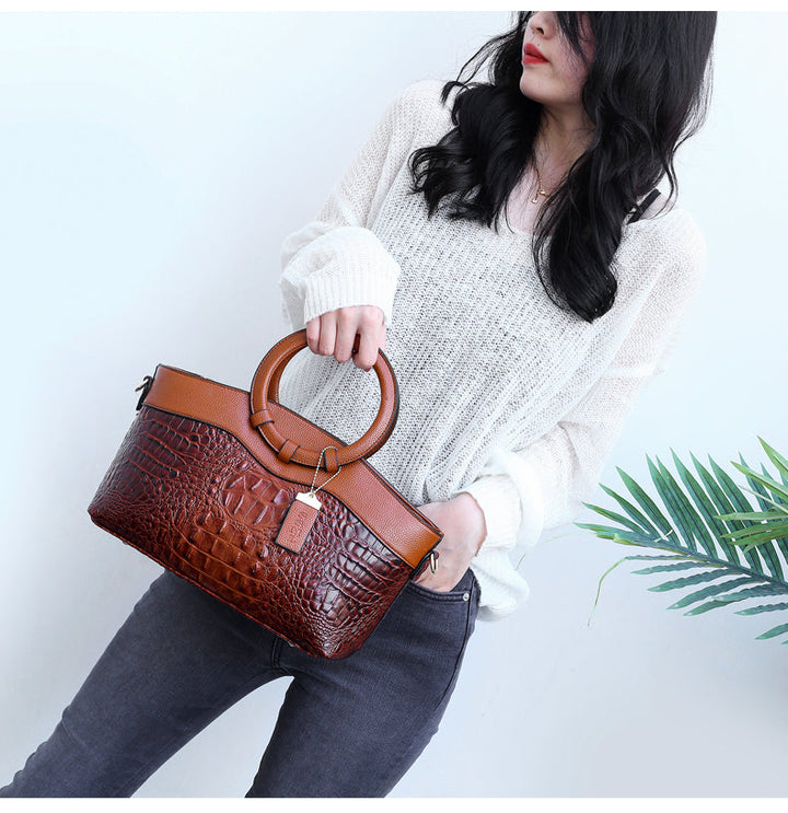 Brown croc-embossed handbag with top handle, front strap detail, and zip closure.
