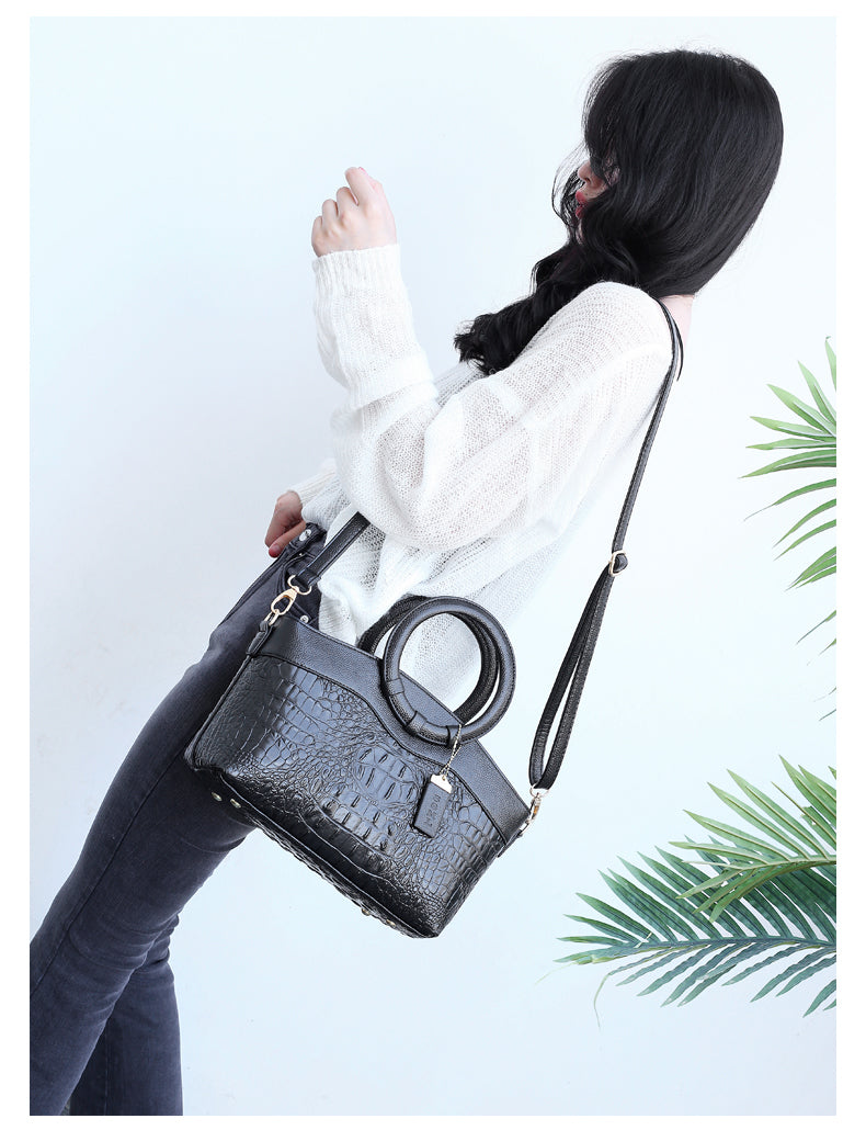 Dark croc-embossed handbag worn crossbody with top handle rings and zip closure.