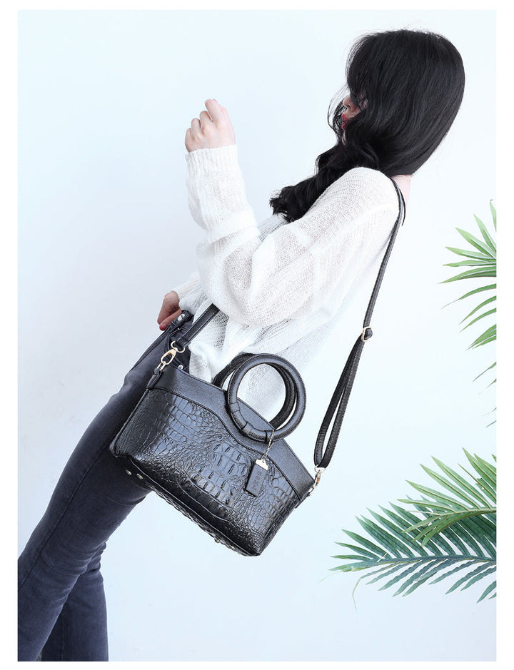 Dark croc-embossed handbag worn crossbody with top handle rings and zip closure.