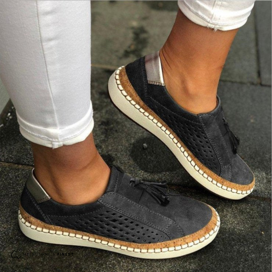 Black orthopedic slip-on shoes with tassel detail, perforated upper, and cream sole