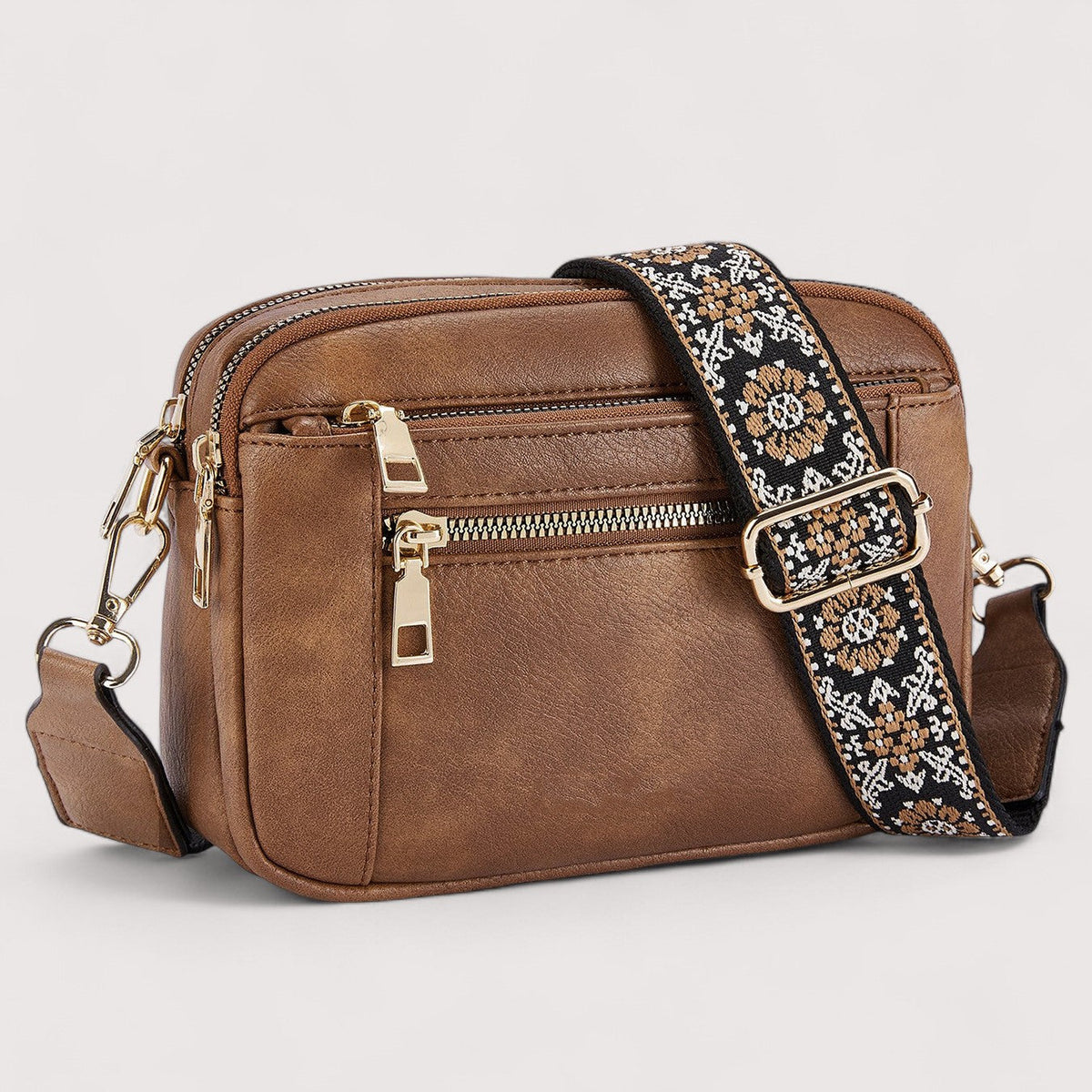 Brown lightweight crossbody bag with top zip, front pocket, and patterned strap.