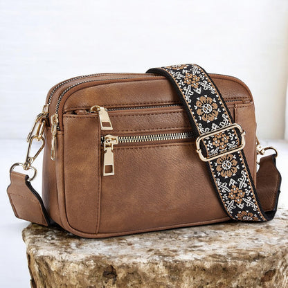 Brown lightweight crossbody bag with top zip and patterned crossbody strap.