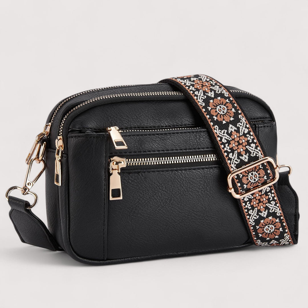 Black lightweight crossbody bag with top zip, front pocket, and patterned crossbody strap.
