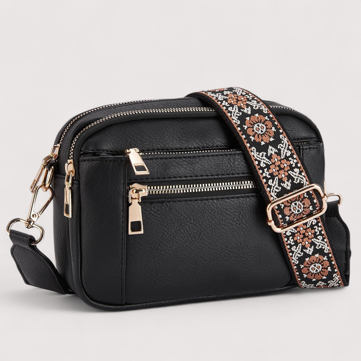 Black lightweight crossbody bag with top zip, front pocket, and patterned crossbody strap.
