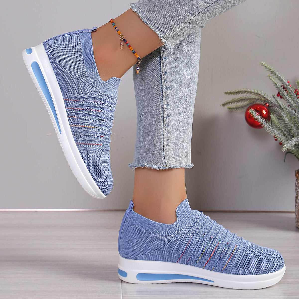Blue knit slip-on sneakers with multicolor stripe detail and white sole, angled view