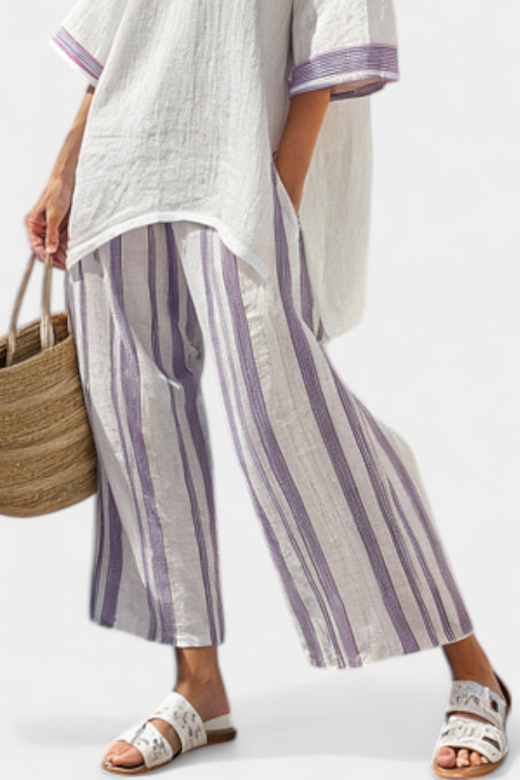 Wide-leg trousers with vertical purple and white stripes, worn with a white tunic hem
