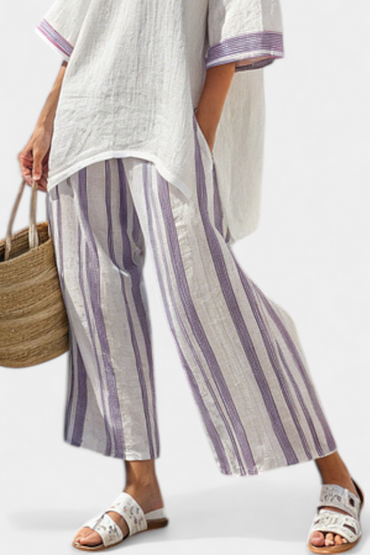 Wide-leg trousers with vertical purple and white stripes, worn with a white tunic hem