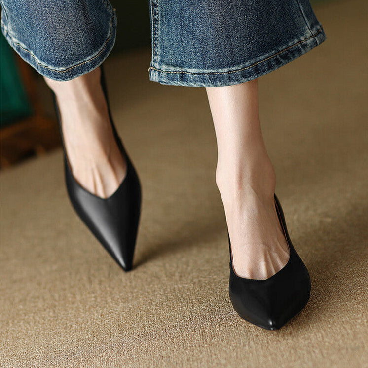 Black pointed-toe pumps on foot with folded blue jeans, low block heel