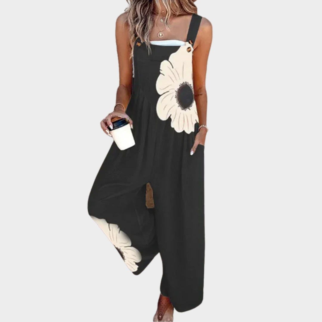 Black sleeveless printed overalls with white daisy motif, wide legs, buttoned straps.
