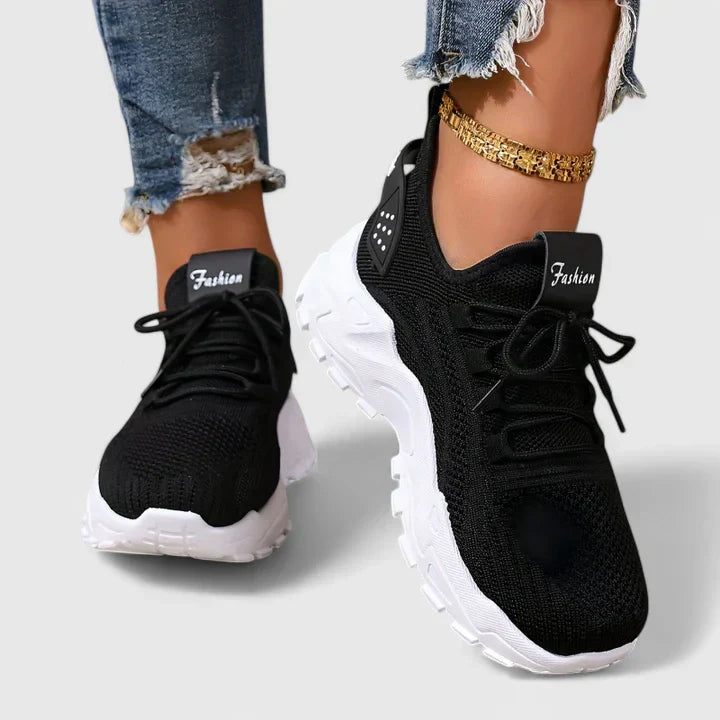 Black orthopedic sneakers with knit upper, lace-up front, and chunky white soles.