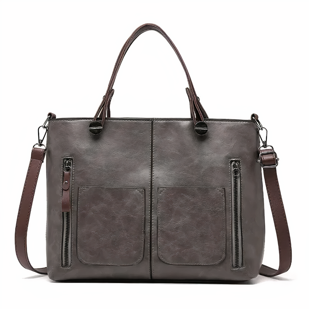 Grey PU leather crossbody tote with twin front pockets, zip pulls, and top handles.