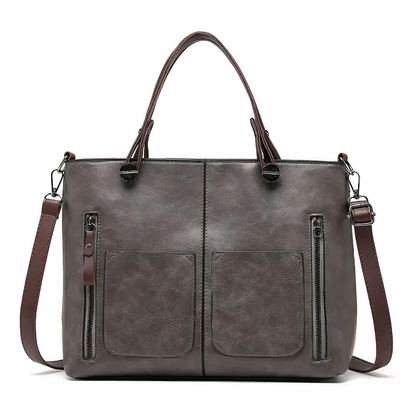 Grey PU leather crossbody tote with twin front pockets, zip pulls, and top handles.