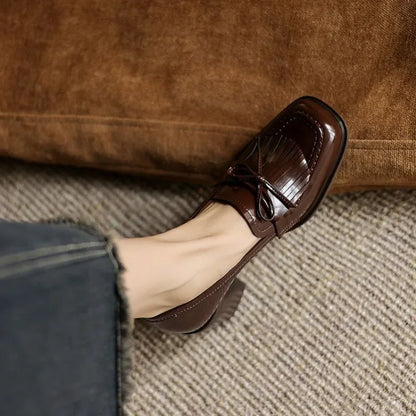 Brown loafer pumps with patent finish, tassel bow detail, and block heel