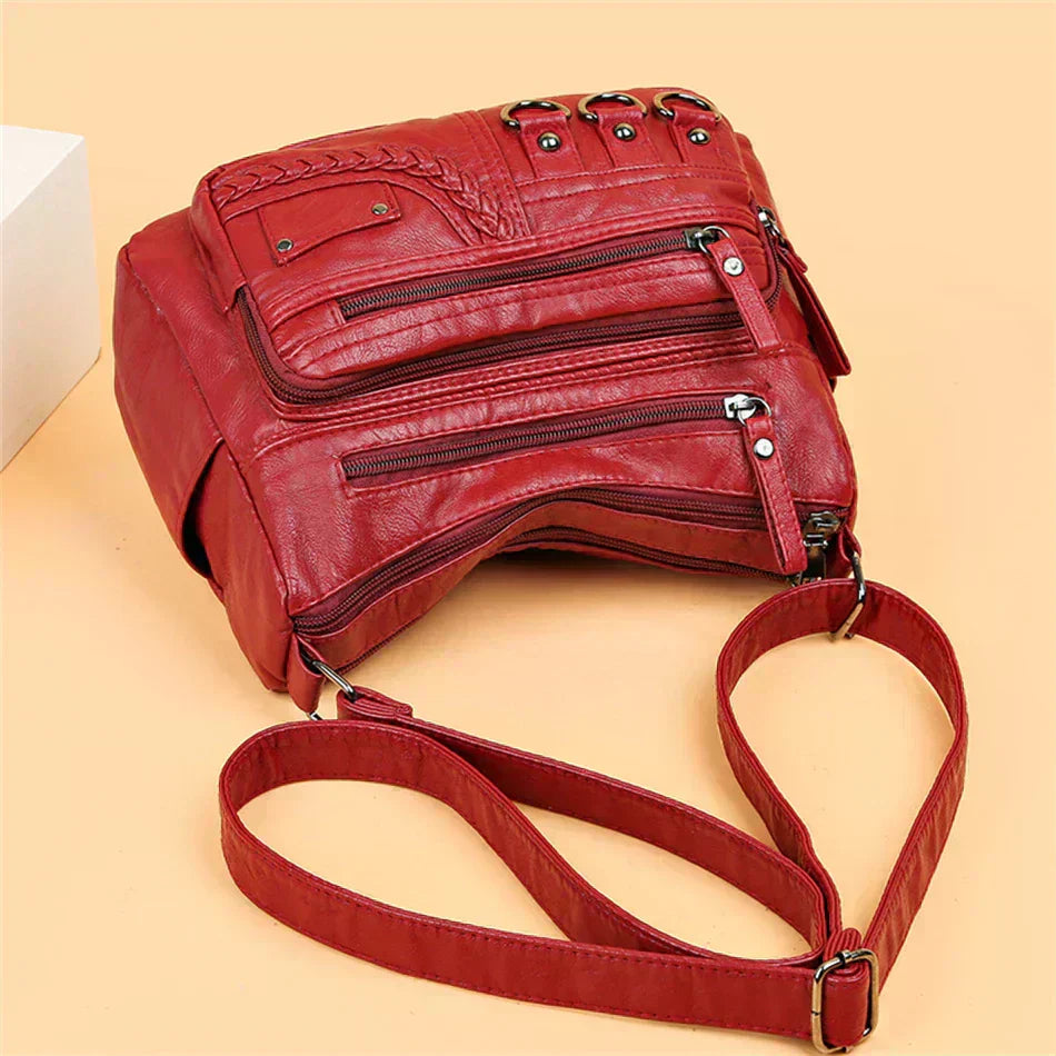 Red leather crossbody bag close-up with layered zipper pockets and adjustable strap